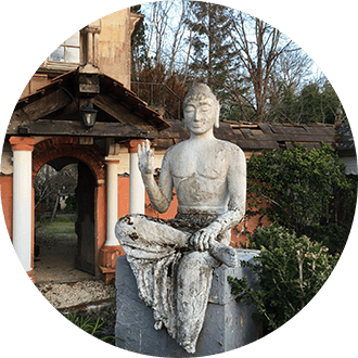Großer Stein-Buddha sitzt in Tempelkomplex, ein Bein lang, das andere angewinkelt, ein Arm schützend nach vorne ausgestreckt.