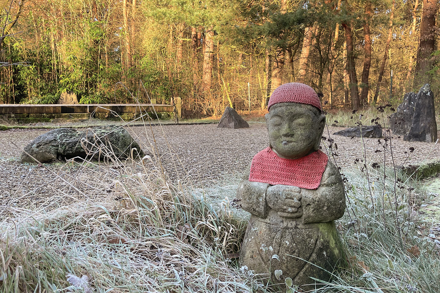 Stehende Mönchsfigur meditiert im Zen-Kiesgarten, im Hintergrund Wald; Atmosphäre ruhig und meditative Retreat-Praxis.