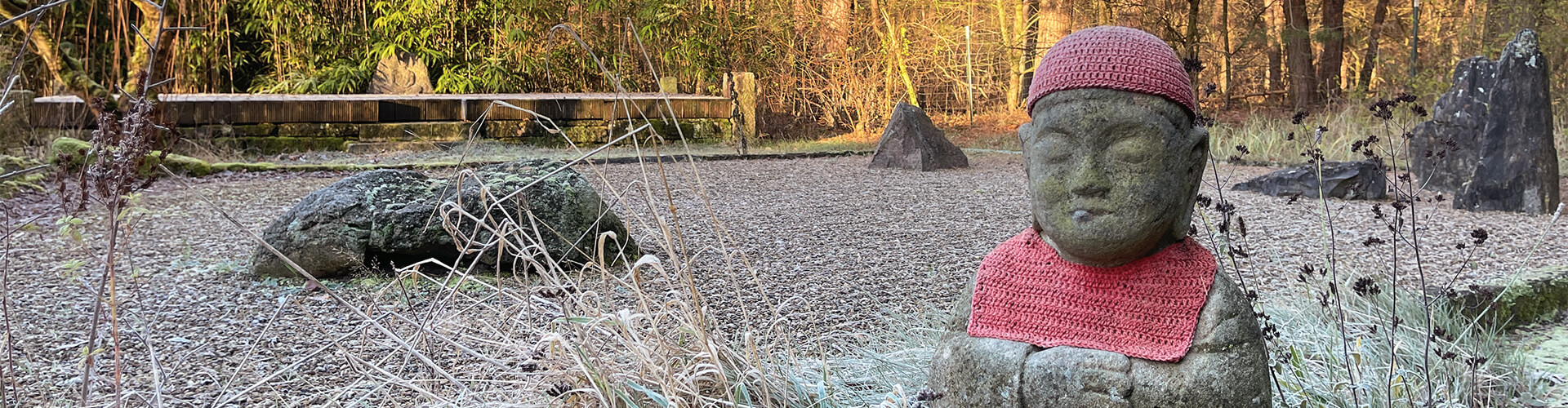 Stehende Mönchsfigur meditiert im Zen-Kiesgarten, im Hintergrund Wald; Atmosphäre ruhig und meditative Retreat-Praxis.