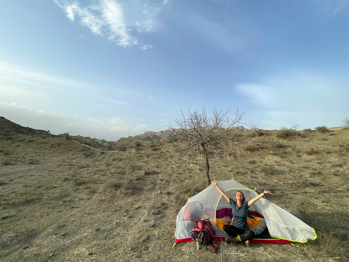 Nirmala sitzt am Zelteingang in Georgiens Wildnis, Arme vor Freude in die Luft gestreckt.