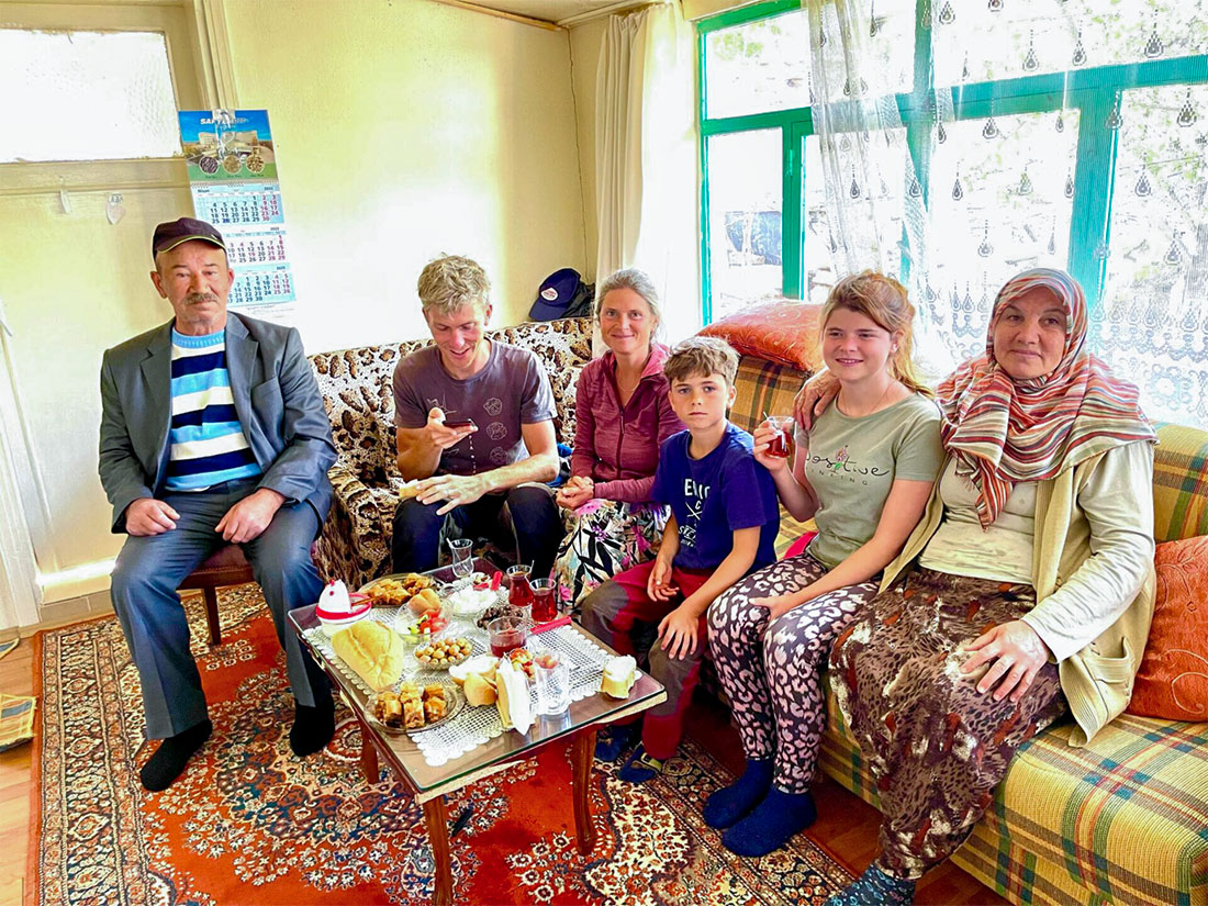 Nirmala sits with her family at the table of Turkish hosts in Turkey, surrounded by food—friendly, lively, cultural.