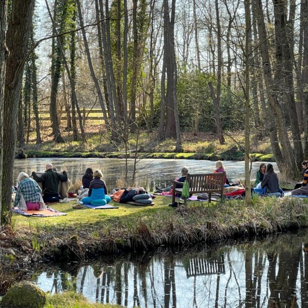 Mehrere Meditierende im Haus der Stille zwischen zwei Seen, auf Halbinsel in Parklandschaft, Meditation im Sitzen und Liegen.