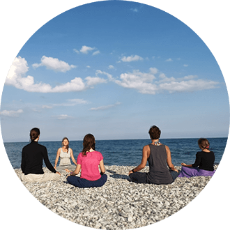 Nirmala leads sitting meditation by the sea, four meditators with their backs to the viewer, looking at the sea, mindful, silent.