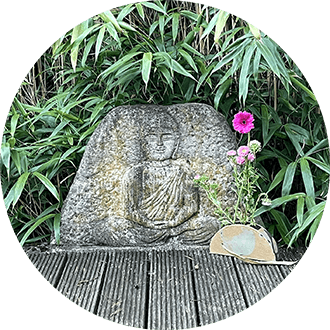 Stone with Buddha relief on meditation platform in ToGenJi Temple, in front of it a pink flower, surrounded by bamboo – mindful, meditative.