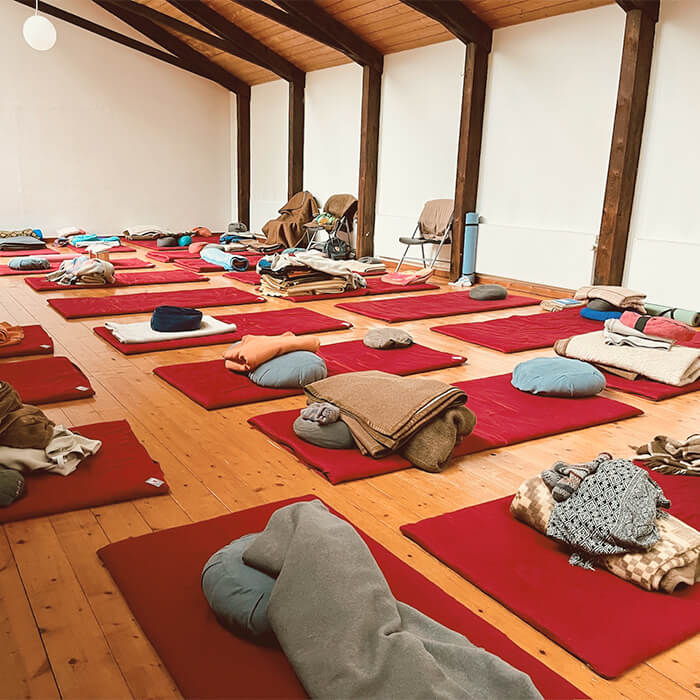 Meditationshalle auf dem Deep Rest Schweigeretreat mit roten Matten und Kissen für traumasensible Meditation im Liegen.