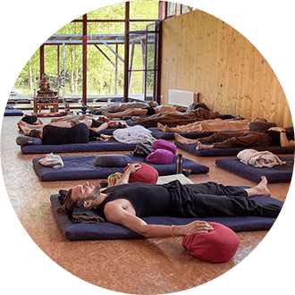 People lie on black mats in the ToGenJi Temple, practicing trauma-sensitive Deep Rest Meditation lying down, Buddha in the background.