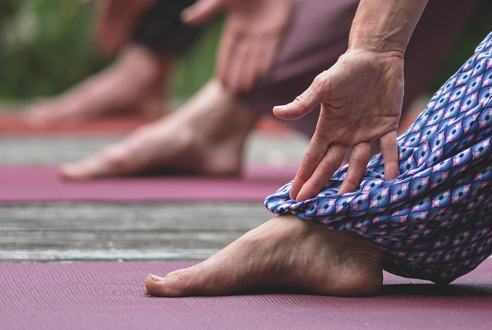 Nahaufnahme von drei Yogamatten, ein Fuß und Arm in Yogahaltung scharf im Vordergrund, dahinter unscharfe Bewegungen.