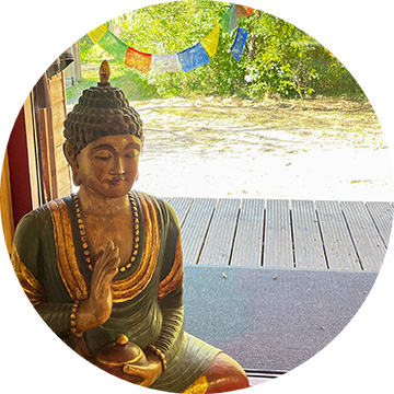 Buddhastatue im verglasten Tempel, im Hintergrund tibetische Gebetsfahnen draußen, Ort der Schweigeretreats.