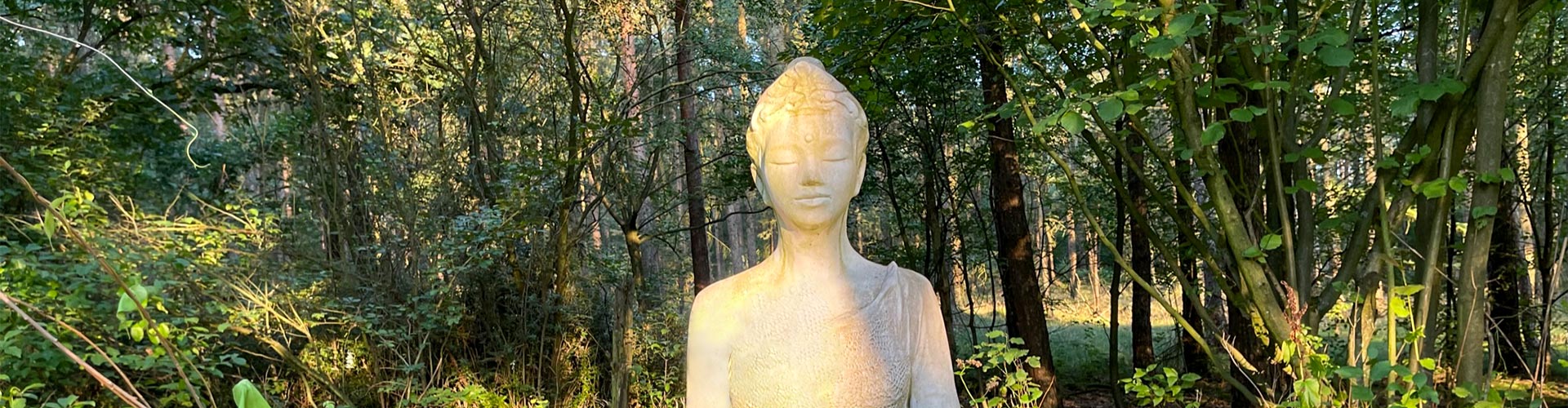 Weiße Tara-Statue im Wald, umgeben von Bäumen, Symbol für Meditation im Liegen auf den achtsamen Schweigeretreats.