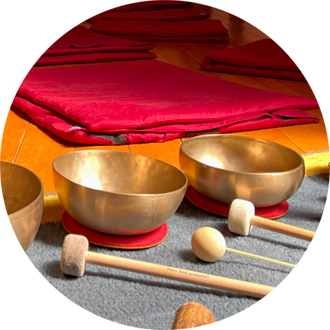 Drei vergoldete Klangschalen mit Schlägeln, dahinter rote Meditationsmatten auf Parkett im Haus der Stille bei Retreat.