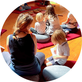 Vier Kinder und eine Mutter sitzen auf roten Meditationsmatten und Kissen, ruhige Familienretreat-Atmosphäre.