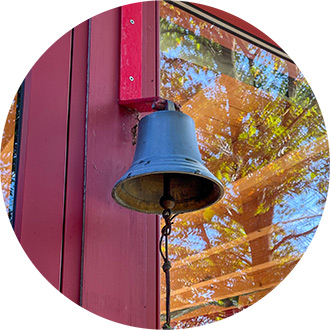 Tempelglocke mit Spiegelung eines herbstlichen Baums im Glas, blauer Himmel im Hintergrund.