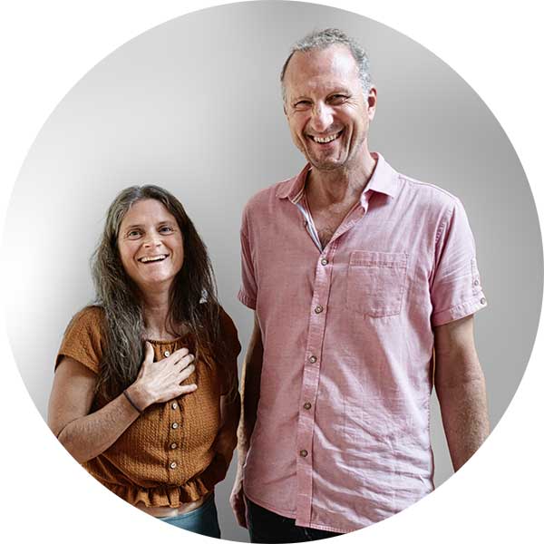 Frithjof Paulig und Nirmala mit Hand auf Herz stehen nebeneinander, blicken in die Kamera, leiten gemeinsam libidinöse Körperarbeit.