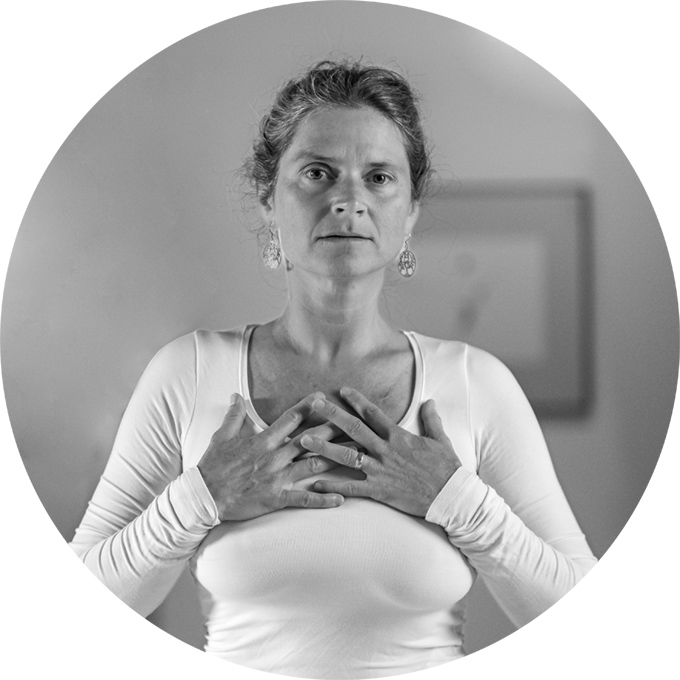 Nirmala facing forward, hands on her chest, looking at the camera, mouth slightly open, hair tied up, silver filigree tree earrings.