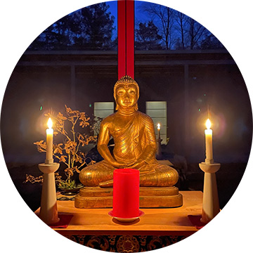 Goldene Buddhafigur im Tempel mit drei Kerzen, verglaste Wand zeigt Nachtwald, meditative Retreat-Atmosphäre.